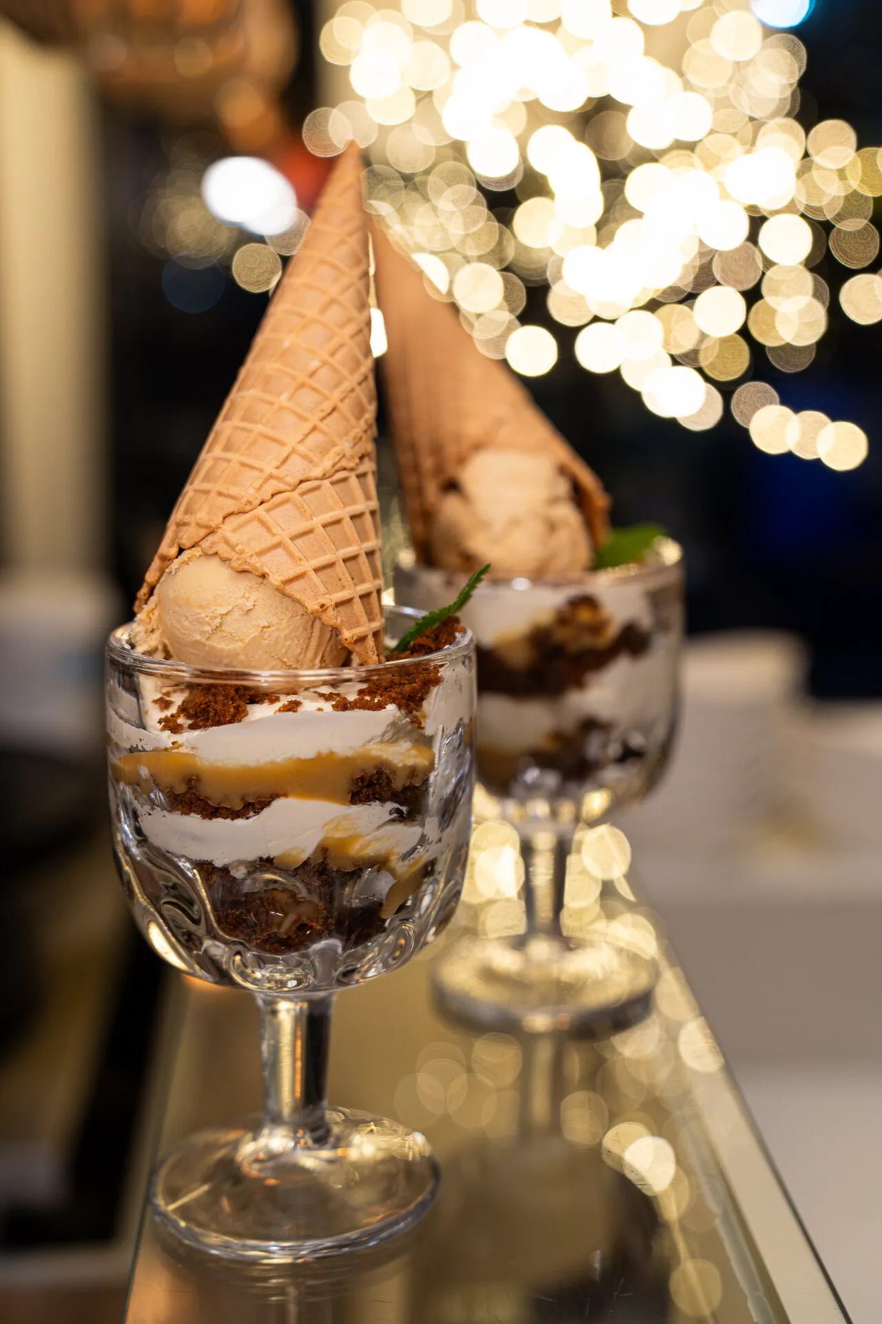 Two festive sundaes topped with waffle cones, Christmas lights behind